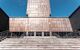 Main entrance to the Costume Museum or Museo del Traje in Madrid, Spain. The building is imposing and almost looks to be made of hammered plates of grey-red metal. There are steps leading up to the entrance, and the sky is clear and blue.