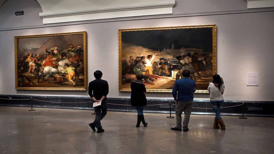 Four visitors stand in front of paintings by Goya in the Prado Museum