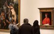 Three visitors stand in front of an oil painting of the Cardinal Raphael. In the painting, he is wearing his red cardinal clothing. There is another painting hung on the wall to the left.