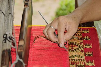 An image of a master tapestry maker, weaving a tapestry with a traditional tool.