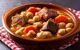 A traditional Spanish chickpea stew (cocido madrileño) is displayed in an earthenware bowl, which has been placed on a red gingham napkin.