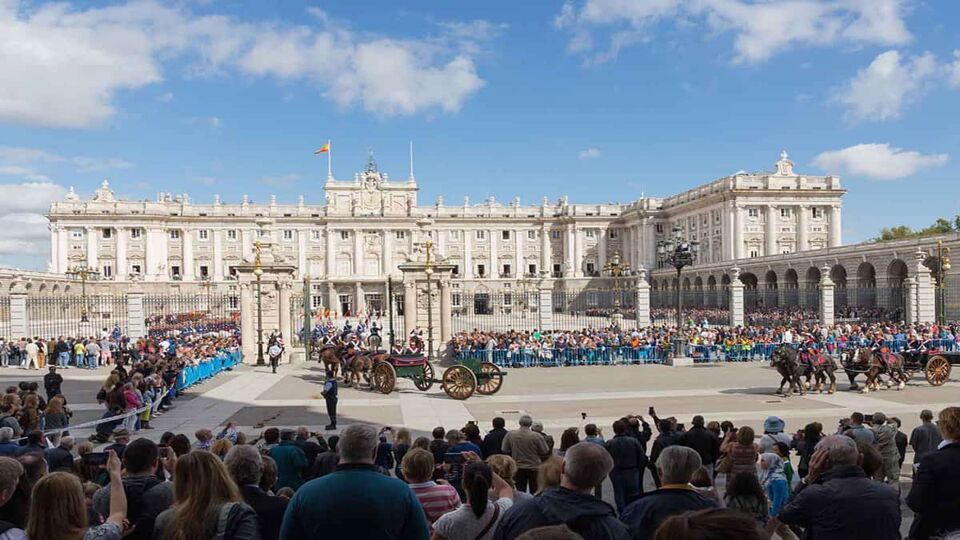 Tourists gather to watch the changing of the guard ceremony. Guards on foot or on horseback line up, and the white palace is visible in the background.