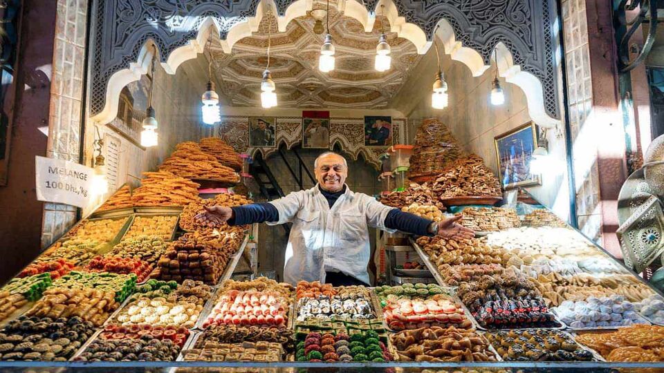 A souk vendor gestures to his wares: piles of dried fruits and candies