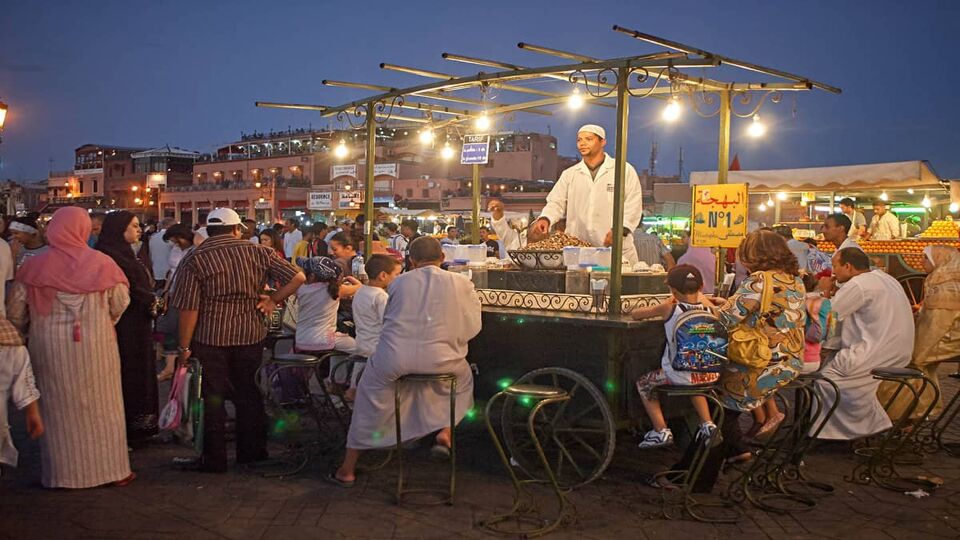 A street food stall in Jemaa El Fna square full of people dining at dusk