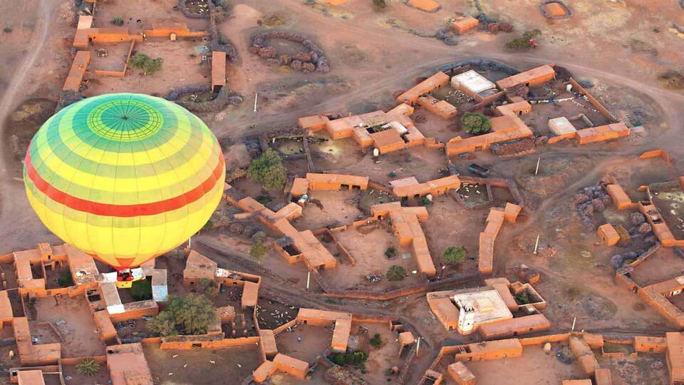 Green, yellow and red hot-air balloon flying over Moroccan village