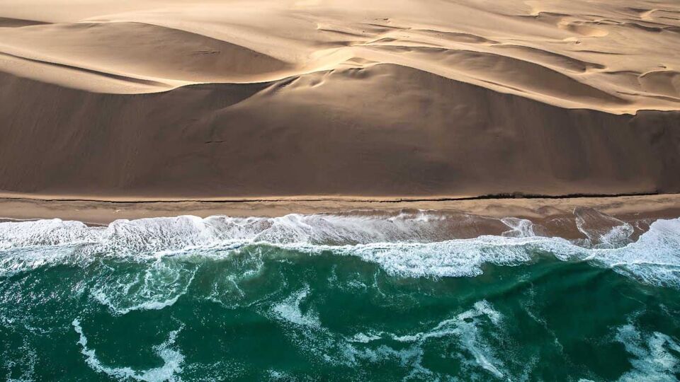 Aerial view of Skeleton coast sand dunes meeting the waves of Atlanic ocean. Skeleton coast, Namibia.