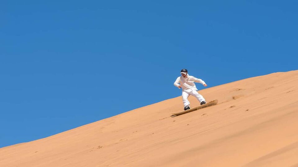 A man on a sand board, sliding down the Swakopmund desert