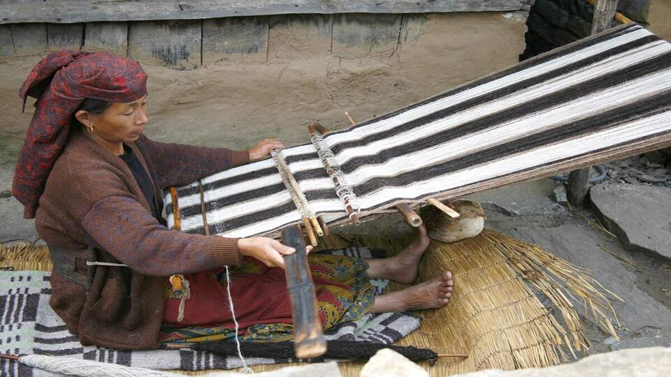 Traditional Gurung woman weaving textile on house terrace.