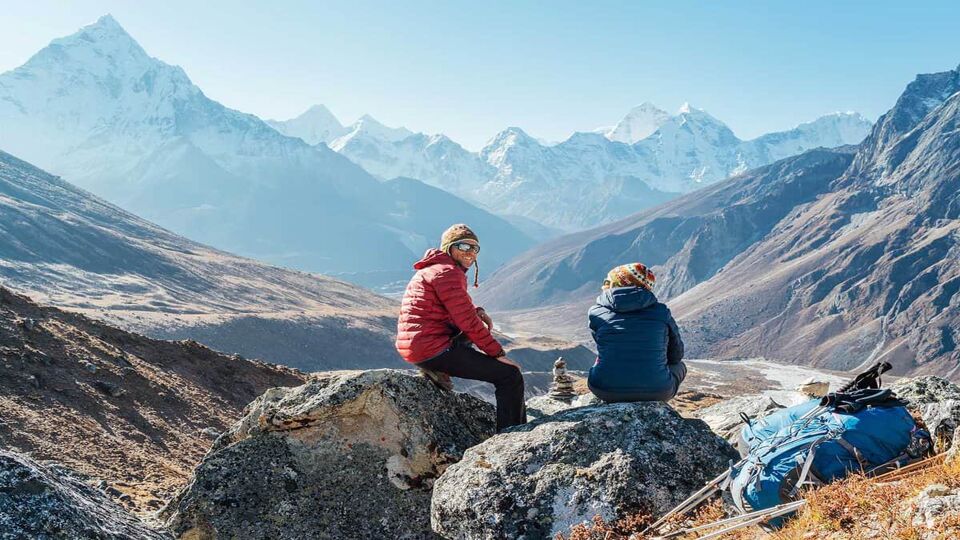Cute Couple resting on the Everest Base Camp trekking route near Dughla 4620m. Man smiling to woman.Backpackers left Backpacks and trekking poles and enjoying valley view with Ama Dablam 6812m peak