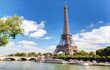 Landscape view of the Eiffel Tower from across the river on a sunny blue day with large clouds