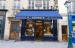 The front view of Stohrer on a street in Paris. The exterior of the shop is painted in navy with a dark blue parasol