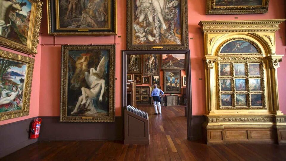 Inside view of the museum where a man is stood inside another room looking around. The room is filled with Gustave's paintings
