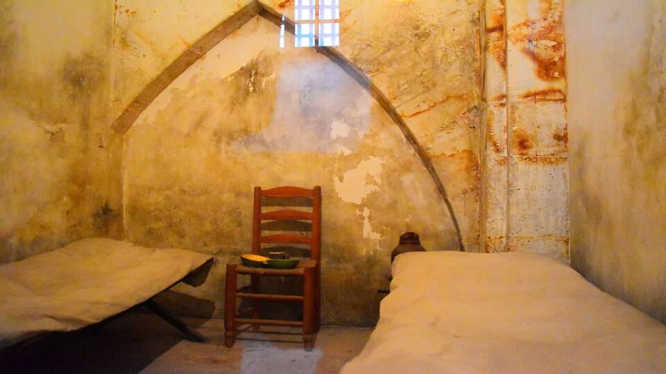 Inside view of a cell in La Conciergerie where are two beds and a chair with dirty walls