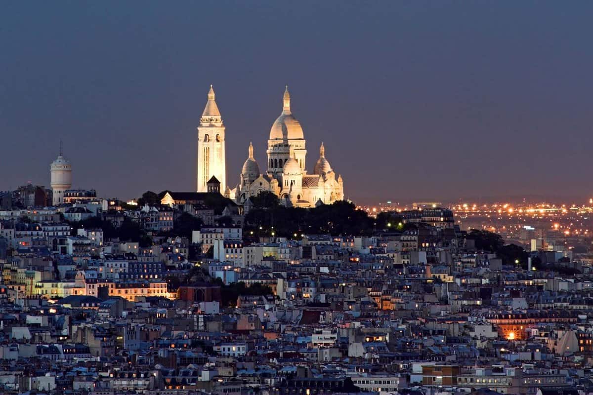 Landscape view of the Sacre coeur at the summit of Montmartre, with the lights of the city illuminating the dark night time sky