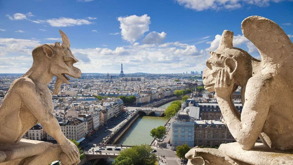 Two gargoyle statues looking at each other on the top of the cathedral, with a beautiful view of the city in the background