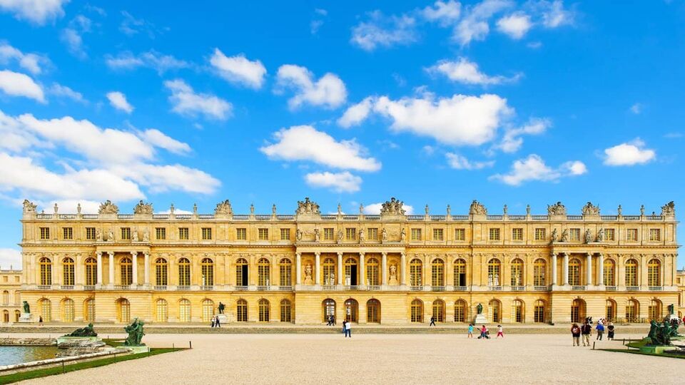 A landscape front view of the Palace of Versailles on a sunny blue day