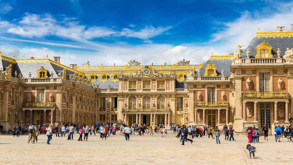 The Royal Court in front of Palace of Versailles with tourists on site and a striking half blue sky with white clouds