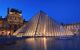 View of the Louvre Pyramid in the evening, illuminating with light from within the pyramid