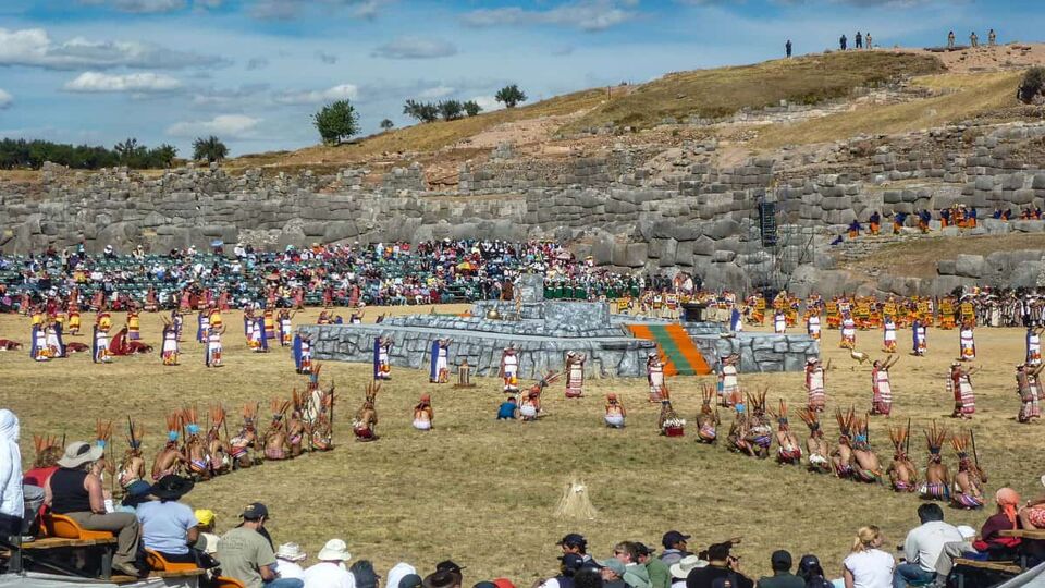 Re-enactment of festival traditions outside among ruins, with spectators sat on grass nearby