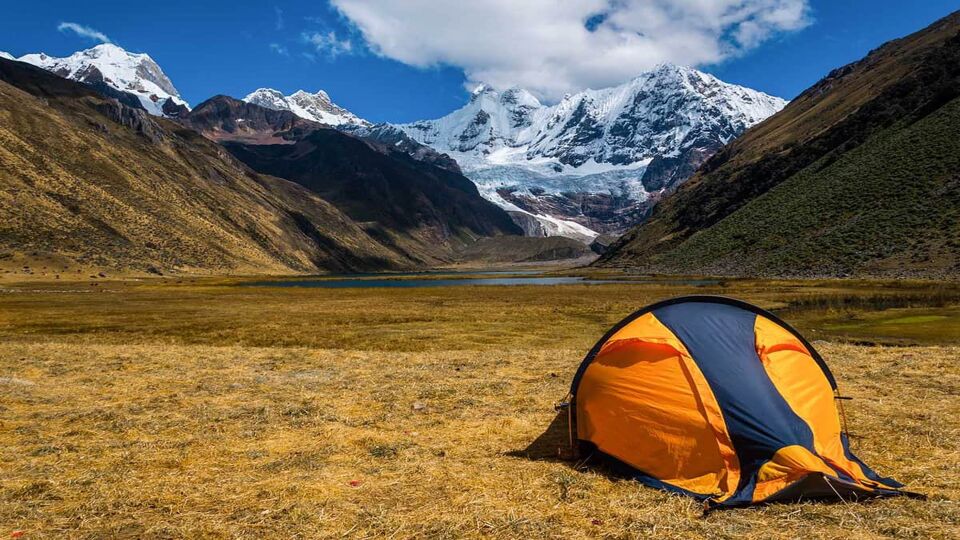 Small orange tent on a flood plain before mountains