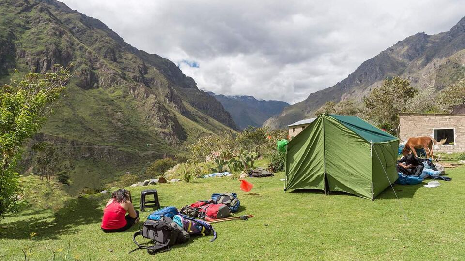 People camping on a grassy area with mountains in the background