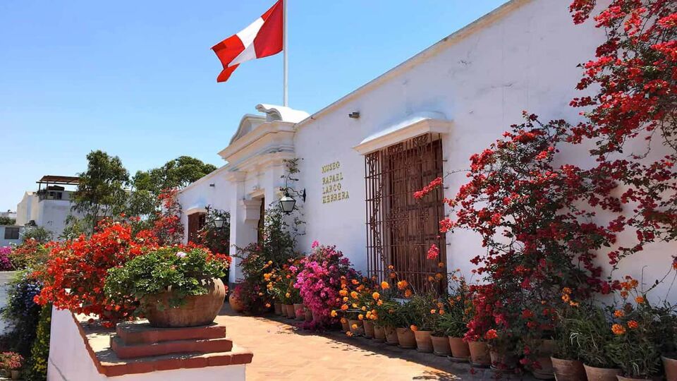 The exterior of the museum, with red-leaved plants and a Peruvian flag
