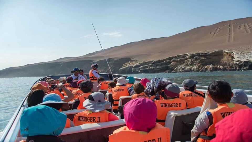 Tourists wear orange life vests in a boat, while passing an island