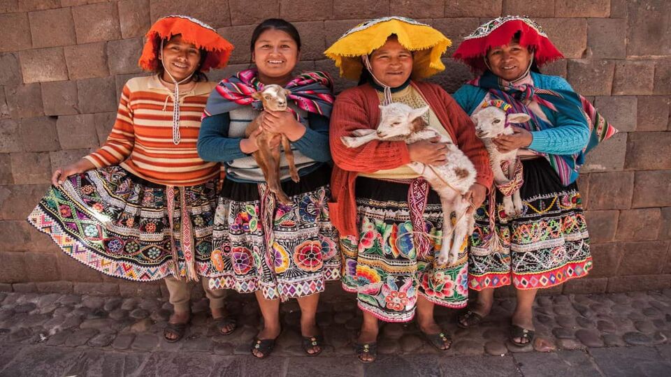 Quechua women show their traditional dress, while three of them hold lambs
