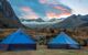 Two tents pitched in front of a sunrise behind mountains