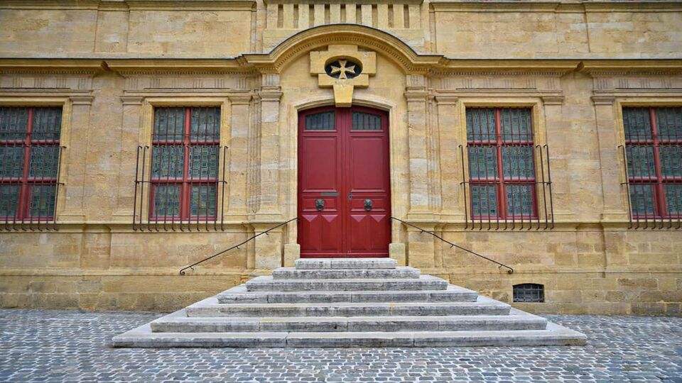 Exterior of the Granet Museum, a low stone building with steps leading up to a red door.