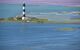 A black and white striped lighthouse sits on land jutting out into the sea