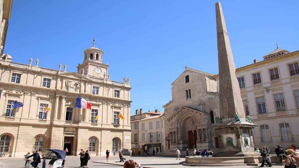 A French flag flying from a building in Place de la Republique, Arles. A momument stands in the square.