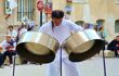 A performer plays two steel pan drums in the street