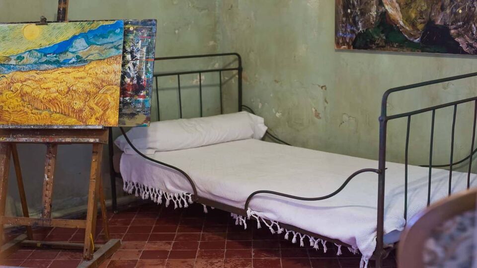 view of a single bed, with green walls and some paintings on an aesel
