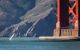 Small sailboat glides under Golden Gate Bridge on a sunny day with base of tower in background