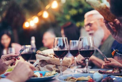 Group eating and drinking red wine at dinner barbecue party outdoor