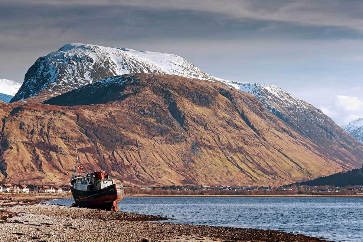 Snow-capped Ben Nevis mountain seen from Fort William. A lake and shipwreck in foreground