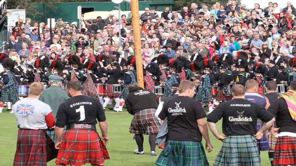 Crowds watching men in kilts tossing cabers at the Highland Games