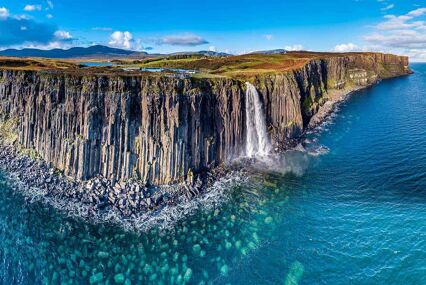 Aerial view of the dramatic coastline cliffs with a large waterfall pouring into the sea