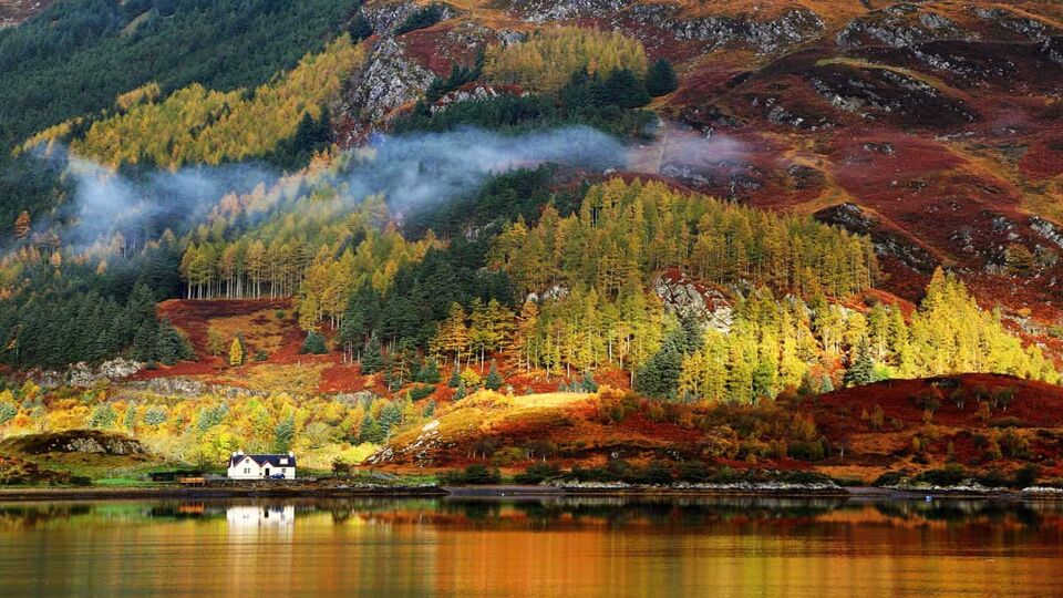 Colourful hillside in autumn with a small house on the shores of a lake in the foreground