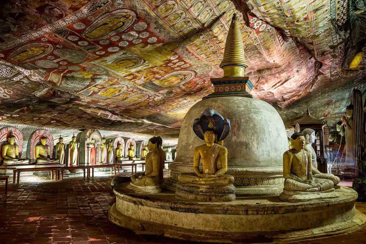 Interior of a cave covered in paintings and full of rows of Buddhas