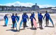 A group of people having a surf lesson walking with surf boards along the beach.