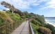 A walking path with greenery on one side, and the sea on the other.