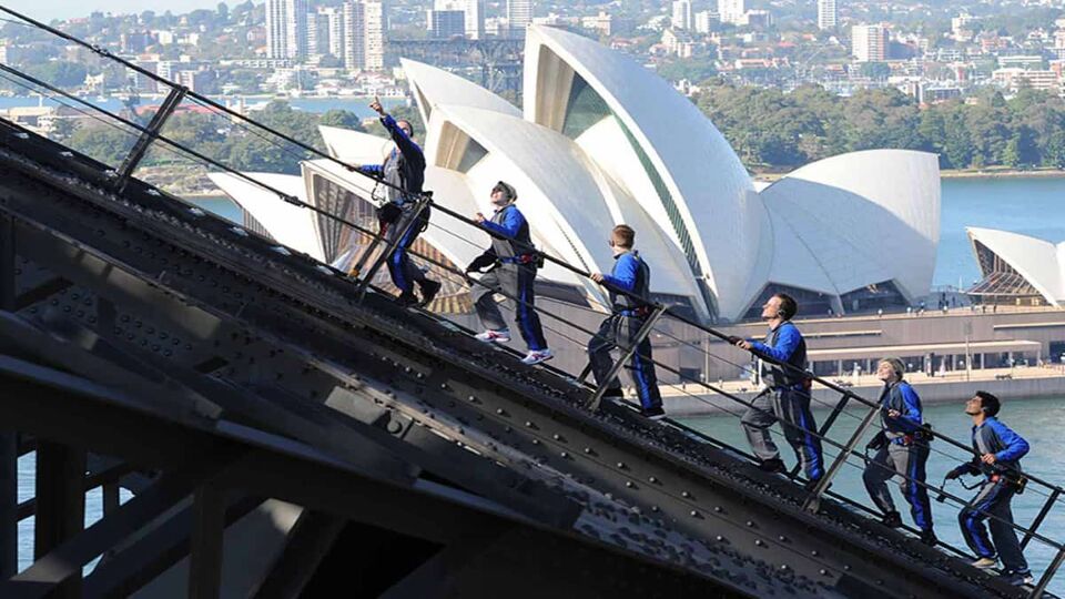 side view of six climbers climbing up, with opera house behindf