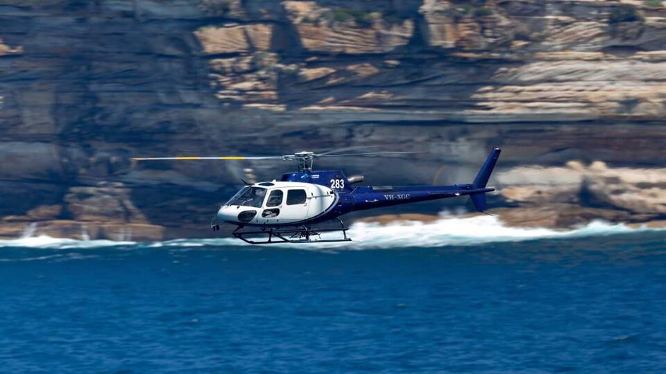 Helicopter flying in front of cliffs over sea
