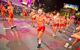 A large group of topless men with short red shorts, dancing as part of the parade at night.