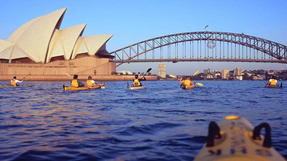 6 People kayaking in front of Sydney Harbour Bridge and the Sydney Opera House on the side. Taken by someone in a kayak.