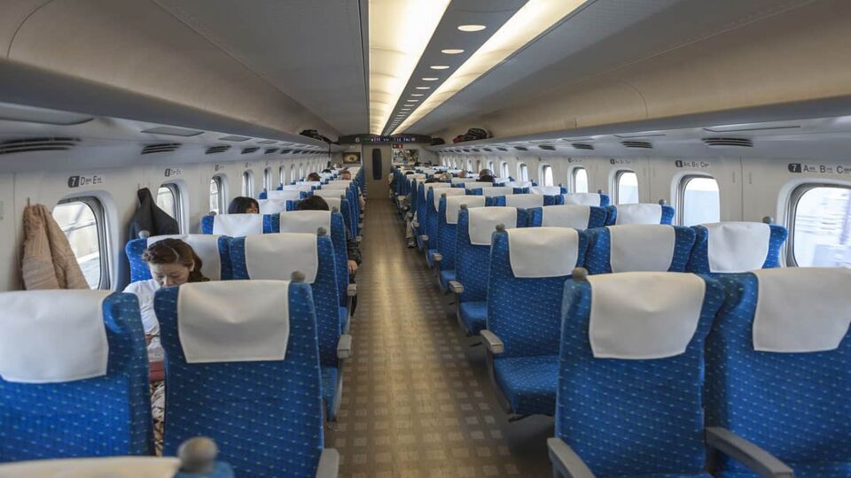 Interior of Japanese bullet train Hikari. Passengers seat in half-empty wagon.