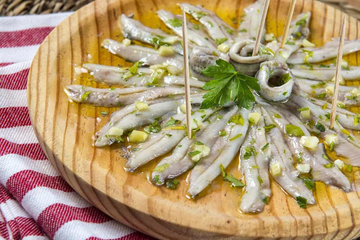 Boquerones – marinated anchovies. close up of a wooden platter of small fish in oil