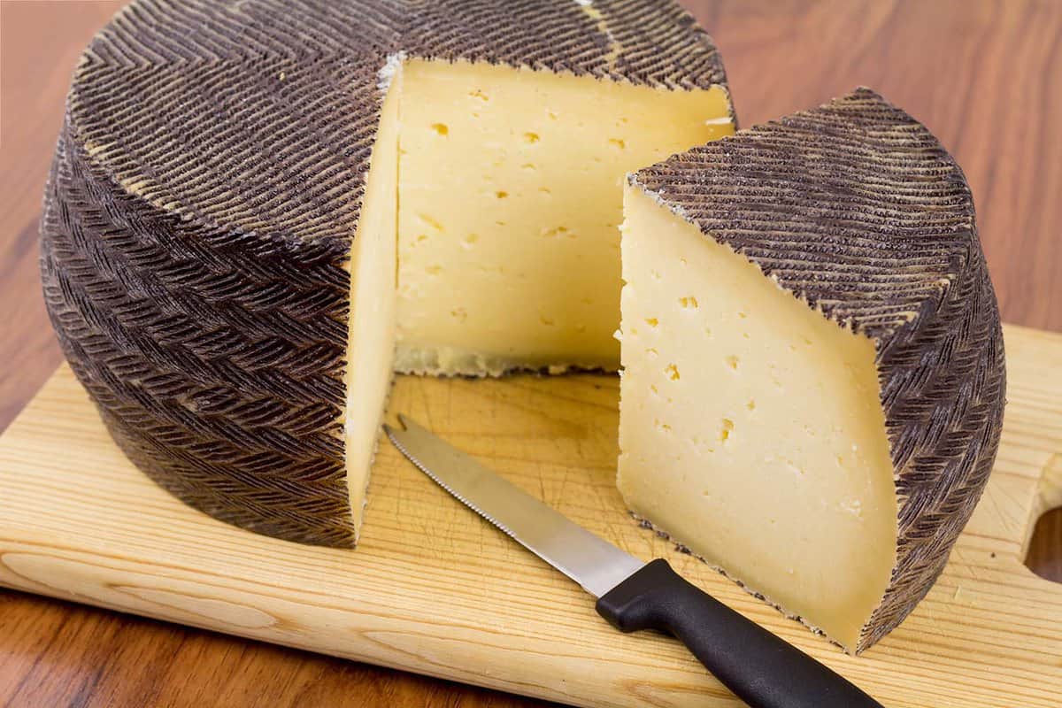 Spanish manchego cheese portion with a special cutting knife on a wooden board